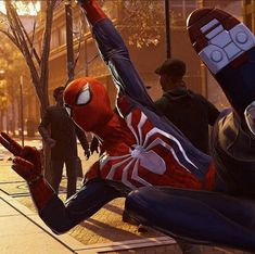 the spider - man is laying on his back in front of some people and pointing at him