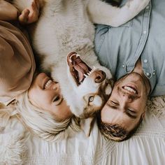 a man and woman laying on top of a bed next to a dog with its mouth open