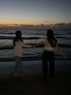 two women are walking on the beach at night with their arms out to each other