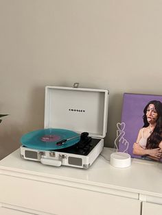 a record player sitting on top of a white dresser next to a painting and potted plant