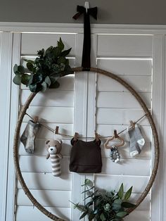 a wreath with baby's clothes hanging on it and some plants in the corner