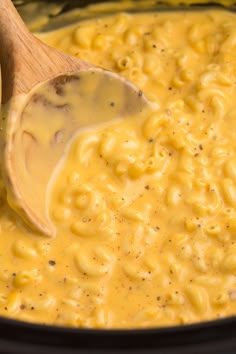 macaroni and cheese being stirred with a wooden spoon