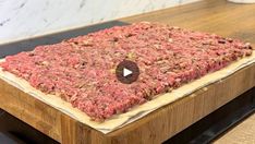 a raw meatloaf on a wooden cutting board with a video player in the background