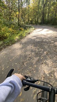 a person riding a bike on a dirt road in the woods with lots of trees