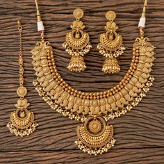 a gold necklace and earring set on a wooden surface, with beads hanging from it