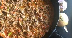 a skillet filled with meat and vegetables on top of a table next to garlic