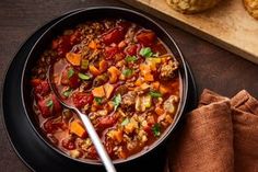 a bowl of soup with meat and vegetables on a wooden cutting board next to muffins