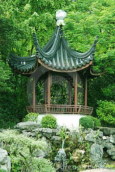 a gazebo in the middle of a garden with rocks and trees around it, surrounded by greenery