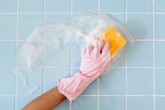 a person's hand in pink rubber gloves cleaning a blue tiled wall