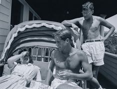 black and white photograph of two men in bathing suits sitting on a porch with an umbrella