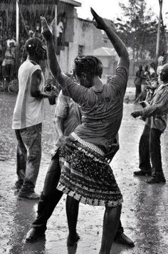 people are dancing in the rain with umbrellas and other people standing around watching them