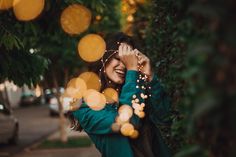 a woman is smiling and holding her head in front of some trees with lights on them