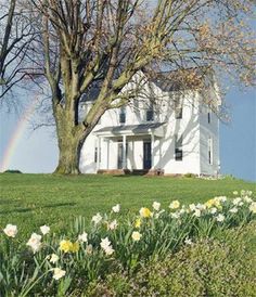 a white house sitting on top of a lush green field next to a rainbow in the sky