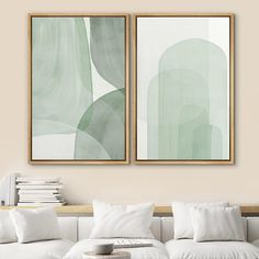 two paintings hanging on the wall above a couch in a living room with white pillows