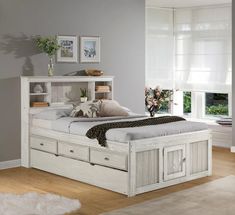 a white bed with drawers underneath it in a room next to a window and rug