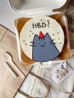 a cake with a cat on it sitting in a box next to utensils