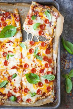 a pizza with pepperoni, cheese and basil on a baking sheet next to fresh basil leaves