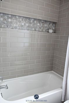 a white bath tub sitting under a window next to a shower curtain and tiled wall