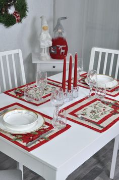 the table is set for christmas dinner with white chairs and red place mats on it