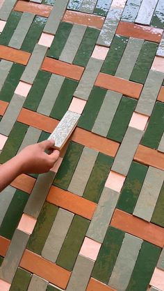 a person is holding a remote control on a mosaic tile floor that has been painted green, brown and pink