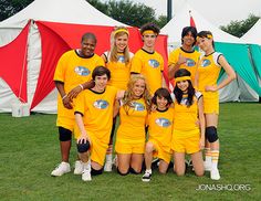 a group of young people in yellow uniforms posing for a photo on the grass with tents behind them