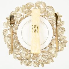 a white plate topped with a golden fork and knife next to a leafy place setting