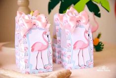 two pink flamingos are wrapped in paper and tied to small gift bags on a table