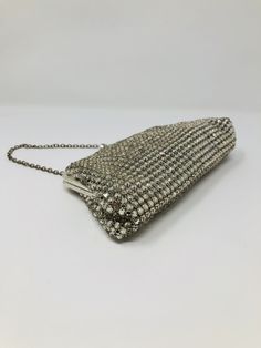 a silver beaded purse on a white surface with a chain attached to the clasp