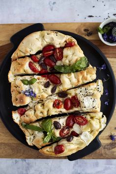 a pizza with tomatoes, olives and mozzarella on a black platter