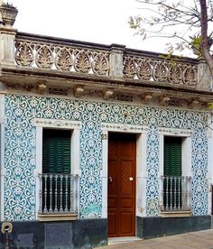 an old building with blue and white tiles on the outside, green shutters and wooden doors