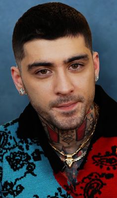 a man with tattoos and piercings on his face looking at the camera while wearing a sweater