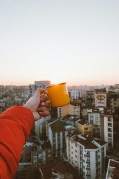 a person holding up a yellow cup in front of a cityscape at sunset