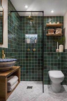 a green tiled bathroom with a toilet, sink and shower stall in the middle of it