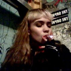 a woman with long hair brushing her teeth in front of graffiti covered wall and street sign