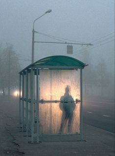 a person standing in front of a bus stop on a foggy day