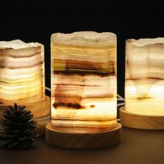 three different types of candles sitting next to each other on a wooden stand with a pine cone in the foreground