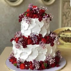 a three tiered cake with white frosting and red berries on top, sitting on a table