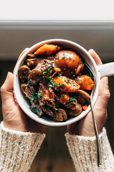 a person holding a white bowl filled with meat and carrots on top of a table