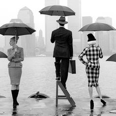 three people standing in the rain with umbrellas over their heads and one woman holding an umbrella