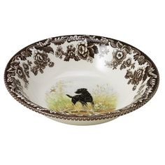 a brown and white bowl with a black dog in the grass on it's side