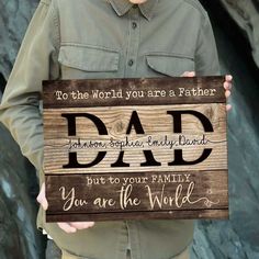 a man holding up a wooden sign that says, to the world you are a father