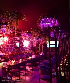 people sitting at tables in a restaurant with purple lighting on the walls and plants hanging from the ceiling