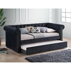 a black daybed with lots of pillows on it in a living room next to a potted plant