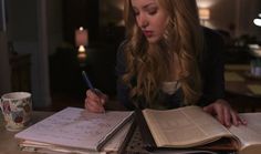 a woman is sitting at a table with books and pens in her hand while she writes