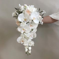 a bridal bouquet with white orchids and pink roses is held by a woman's hand