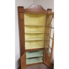 an old fashioned wooden cabinet with shelves and glass doors on the front, in a corner