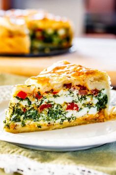 a slice of quiche with spinach and cheese on a plate next to another dish