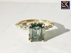 an emerald colored ring with diamonds on the sides and side stones in gold plated setting