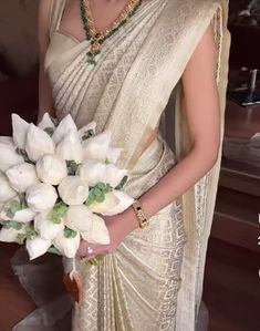 a woman wearing a white sari holding a bouquet of flowers in her left hand