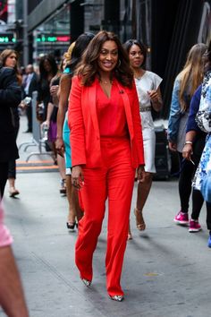 a woman in an orange suit walking down the street with other people on either side